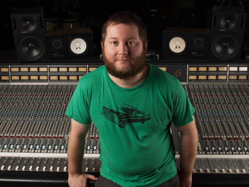 A man in a green shirt standing in front of a mixing desk.