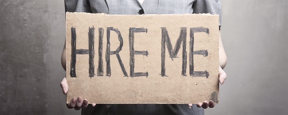 A woman holding up a cardboard sign that says hire me.