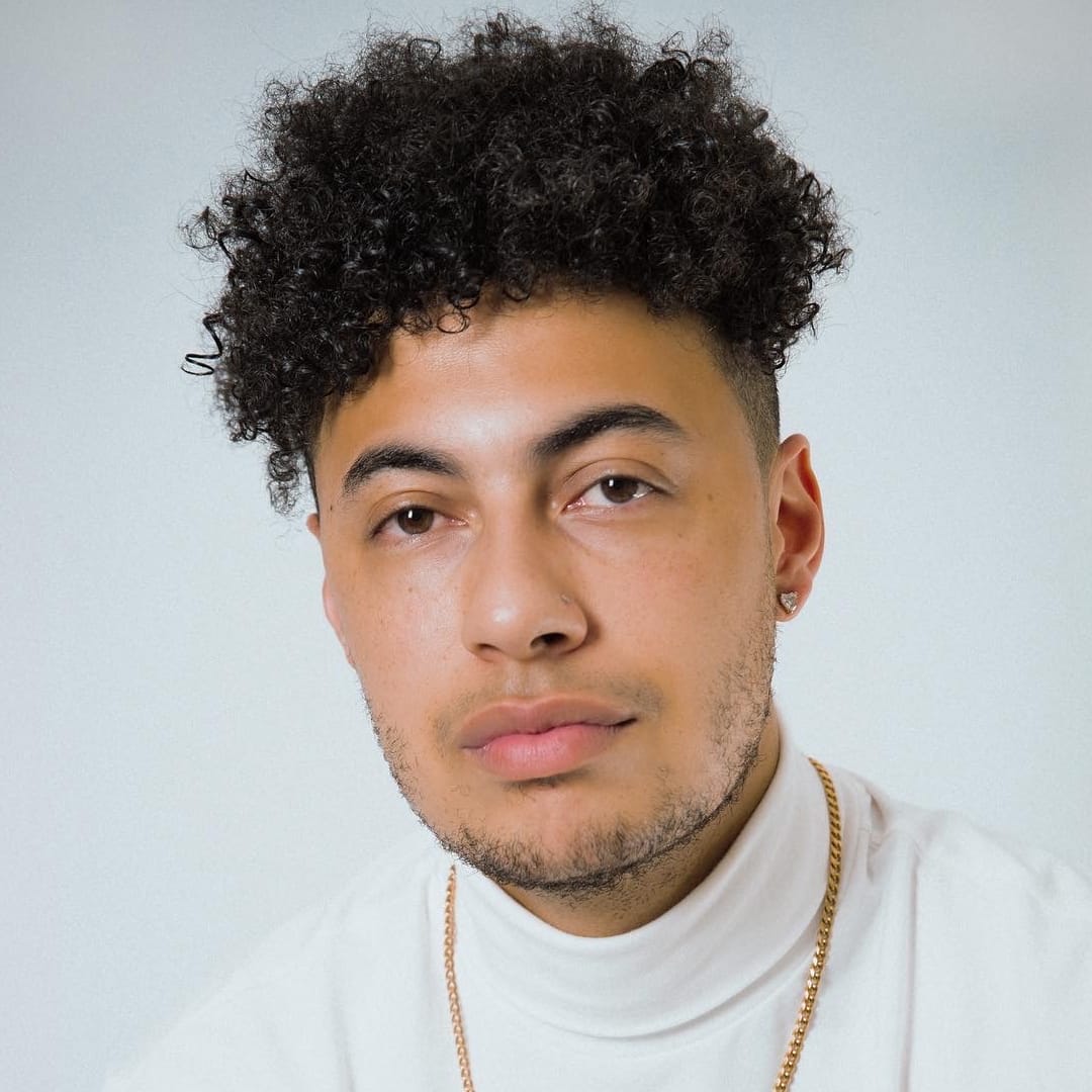 A man in a white turtle neck shirt with curly hair.