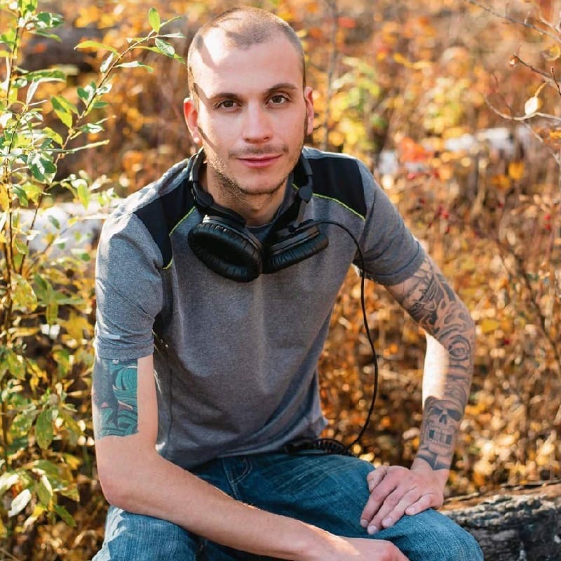 A man in headphones sitting on a log in the woods.