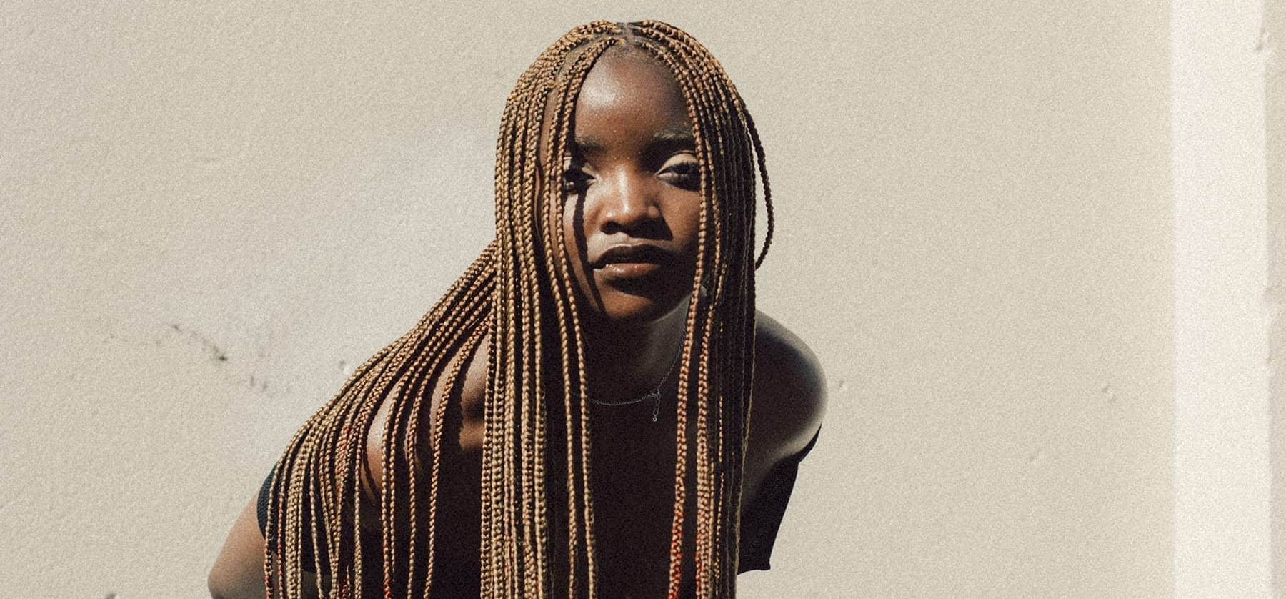 A woman with long braids leaning against a wall.