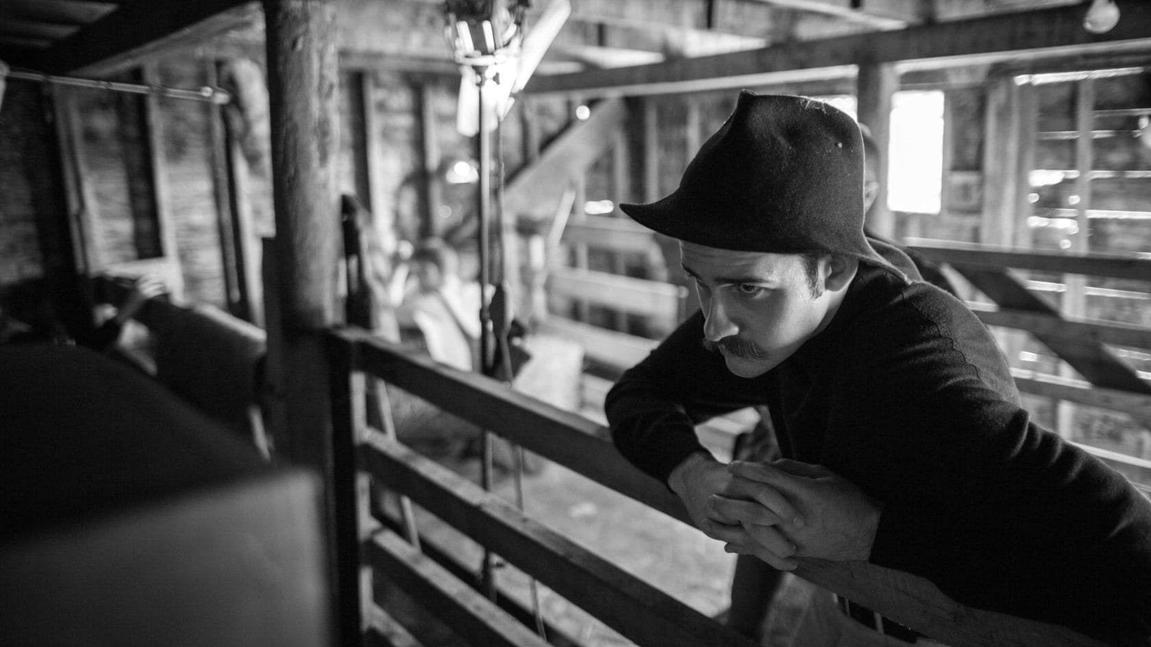 A man leaning against a fence in a barn.