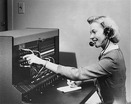 A woman in a headset is working on a telephone system.