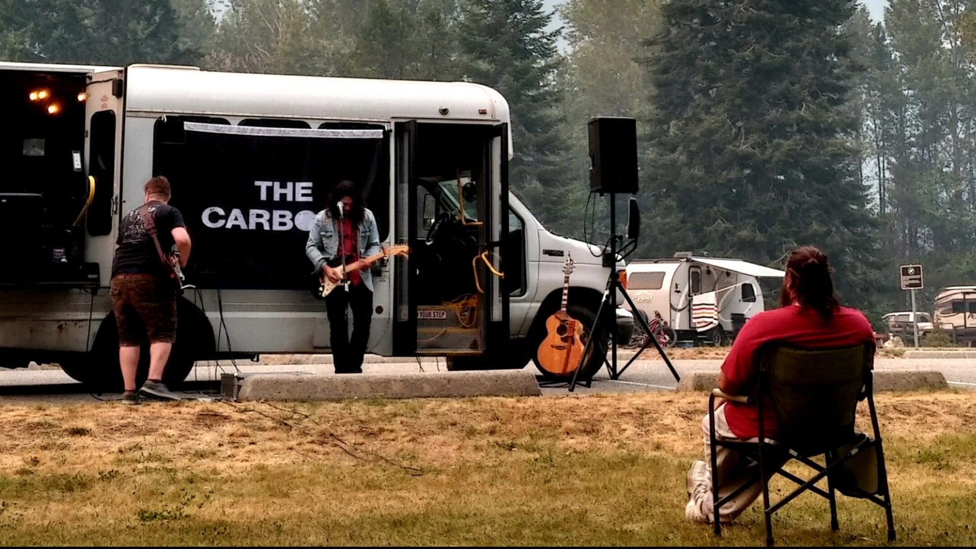 A group of people sitting in chairs in front of a camper van.