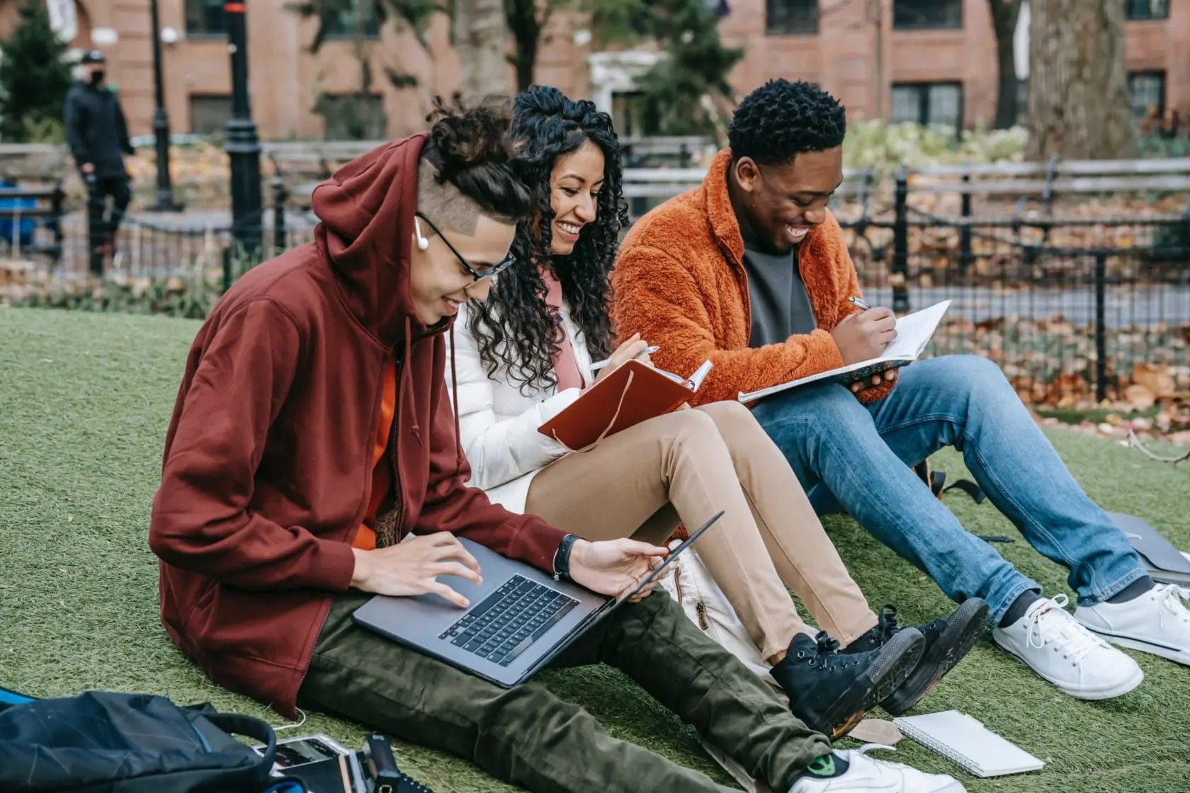 A group of college students sitting on the grass and working on their laptops.