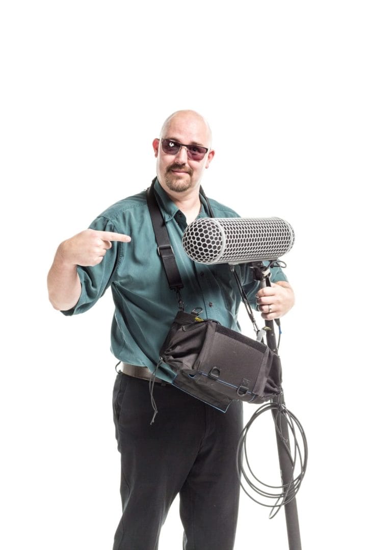 A man holding a microphone and pointing to the camera.