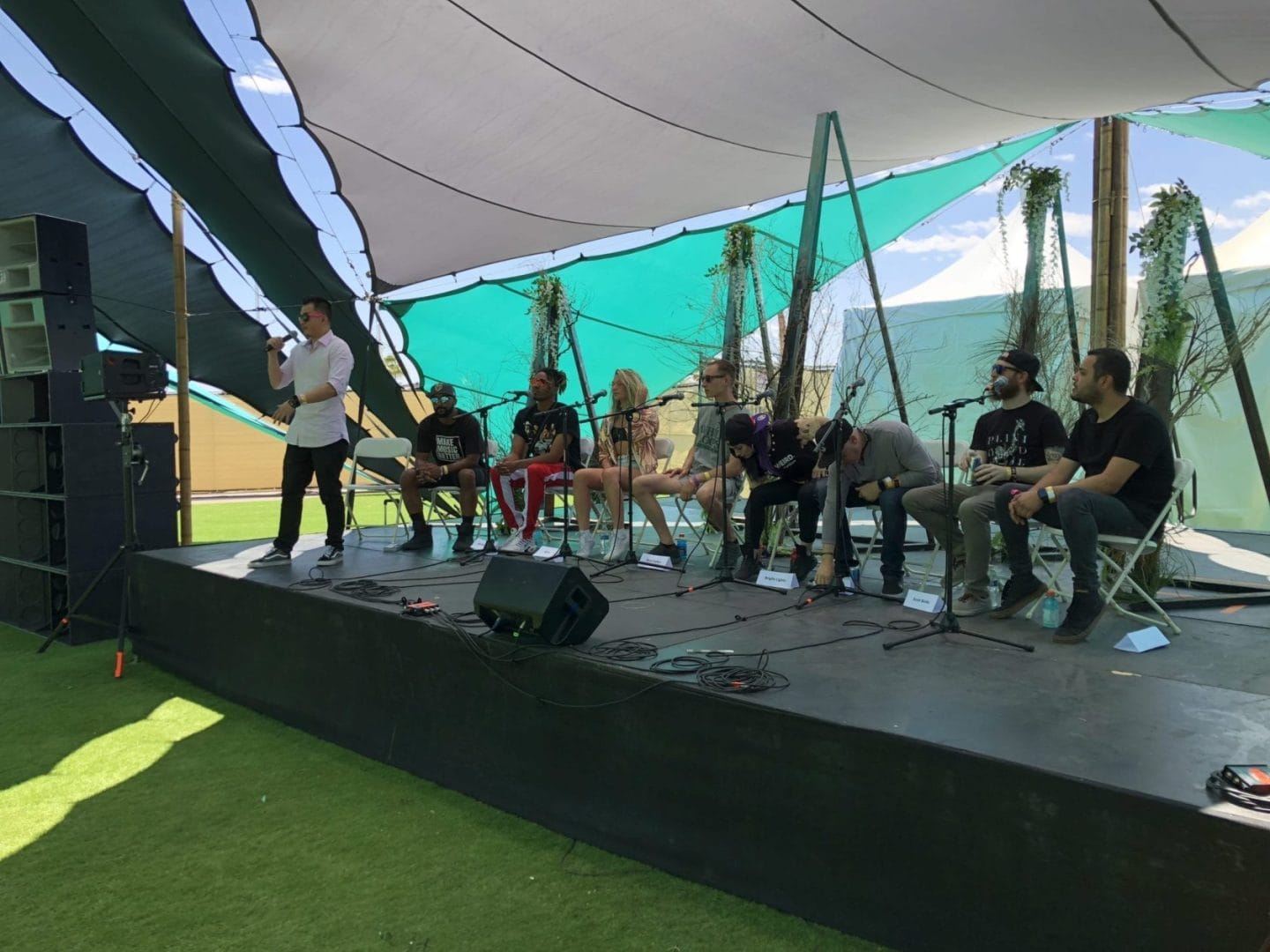 A group of people sitting on a stage in front of a tent.