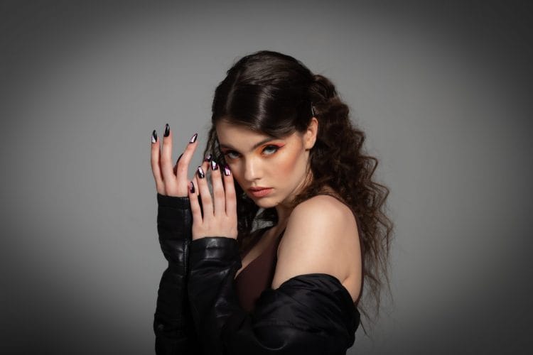 A young woman with long nails posing on a gray background.