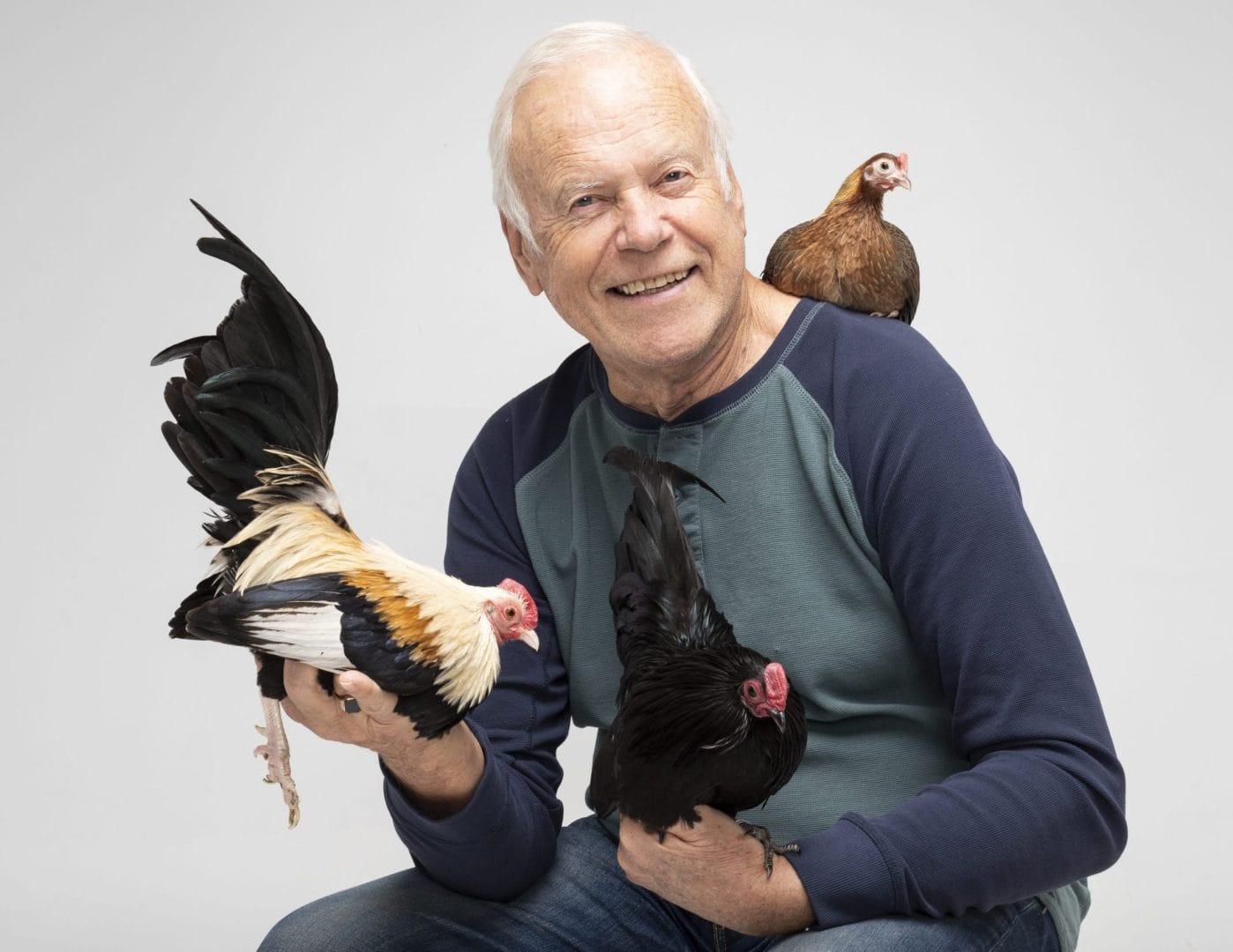 An older man holding a rooster and two chickens.