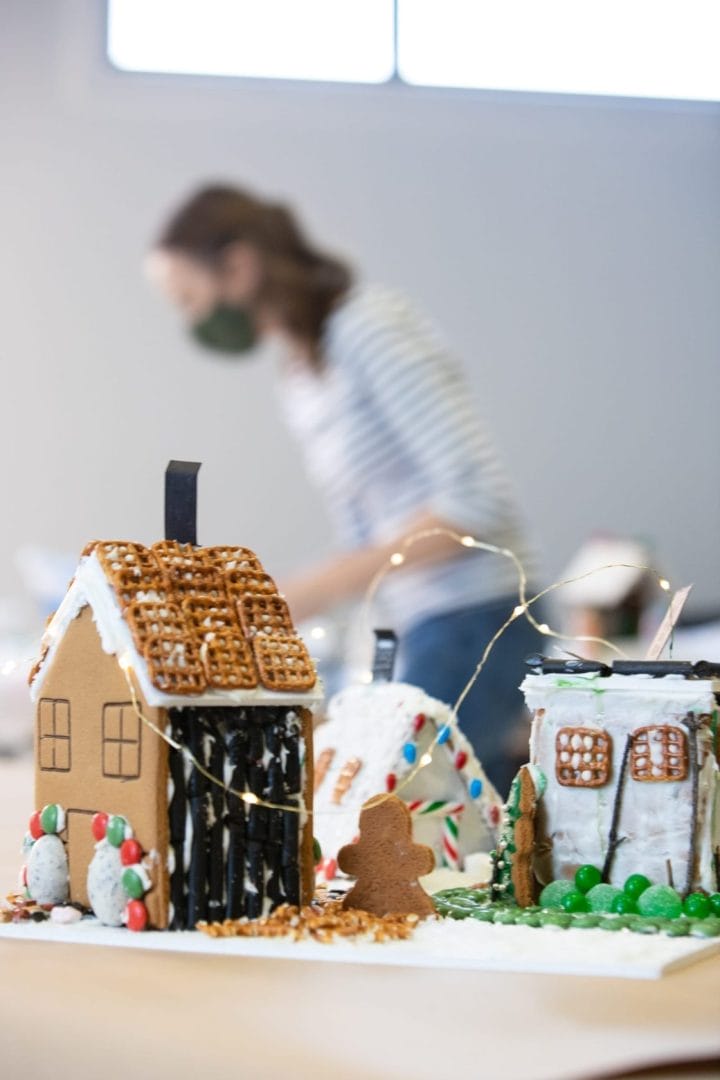 A woman is standing in front of a gingerbread house.