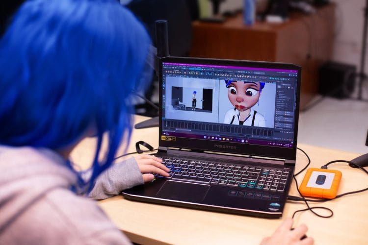 A girl with blue hair is using a laptop.