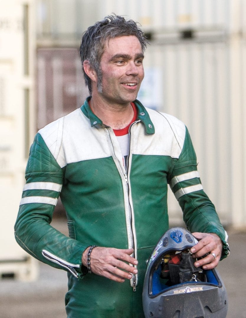 A man in a green and white motorcycle jacket holding a helmet.