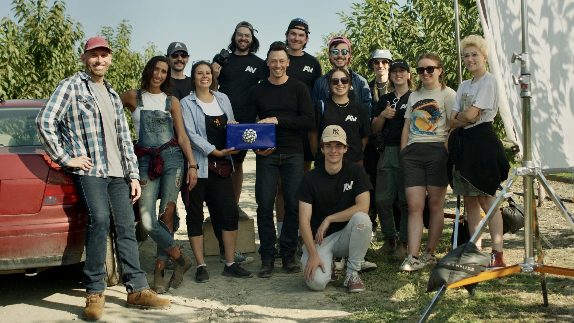 Behind the Lens: The Rise of AV Media – A Journey from Graduation to Award-Winning Filmmakers. A group of individuals stands beside a car in an orchard, symbolizing the collaborative journey from graduation to success in filmmaking.