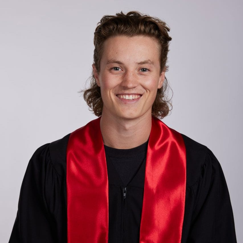 A young man wearing a graduation gown and red sash.