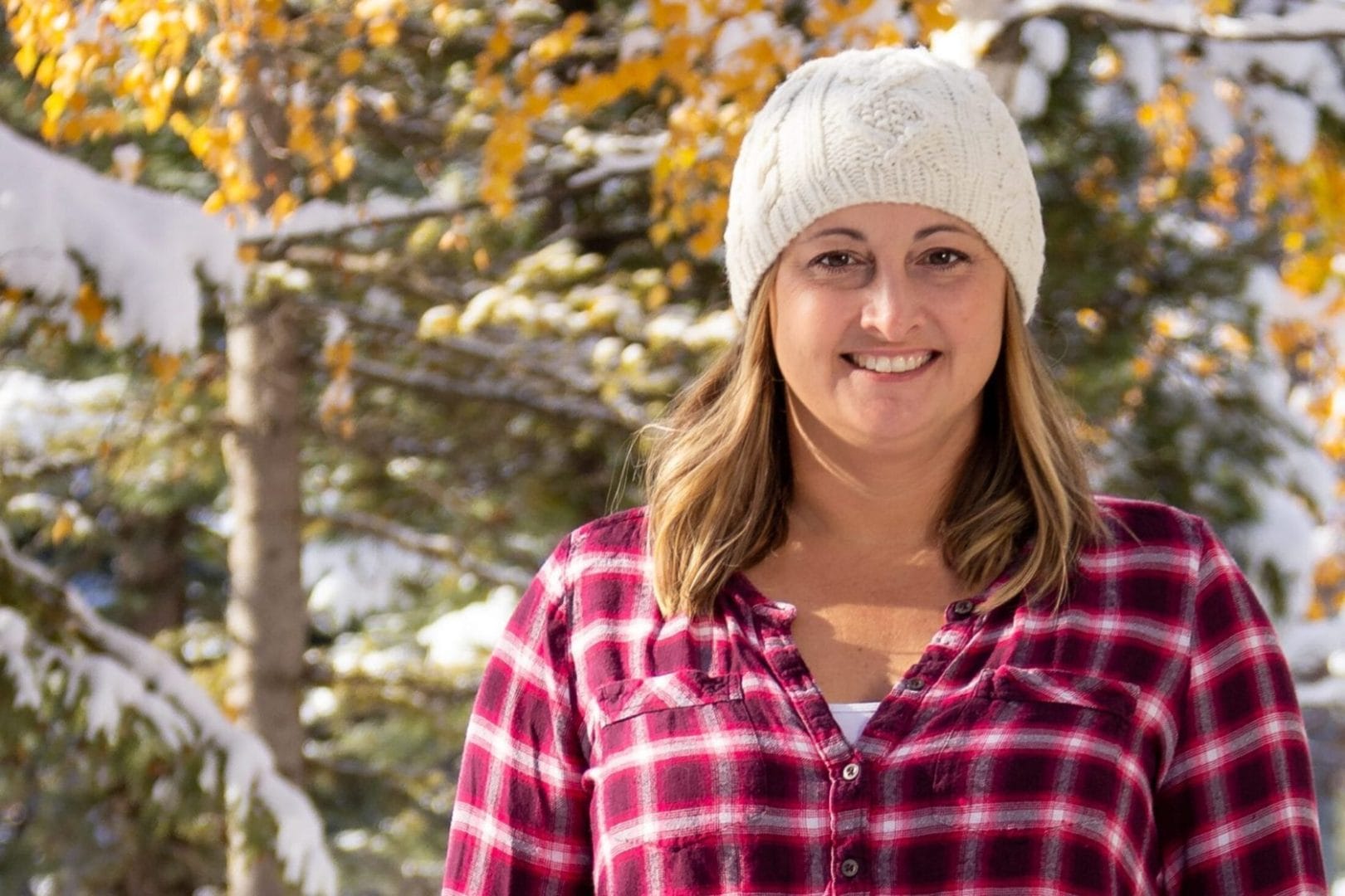 A woman wearing a plaid shirt and a beanie in the snow.