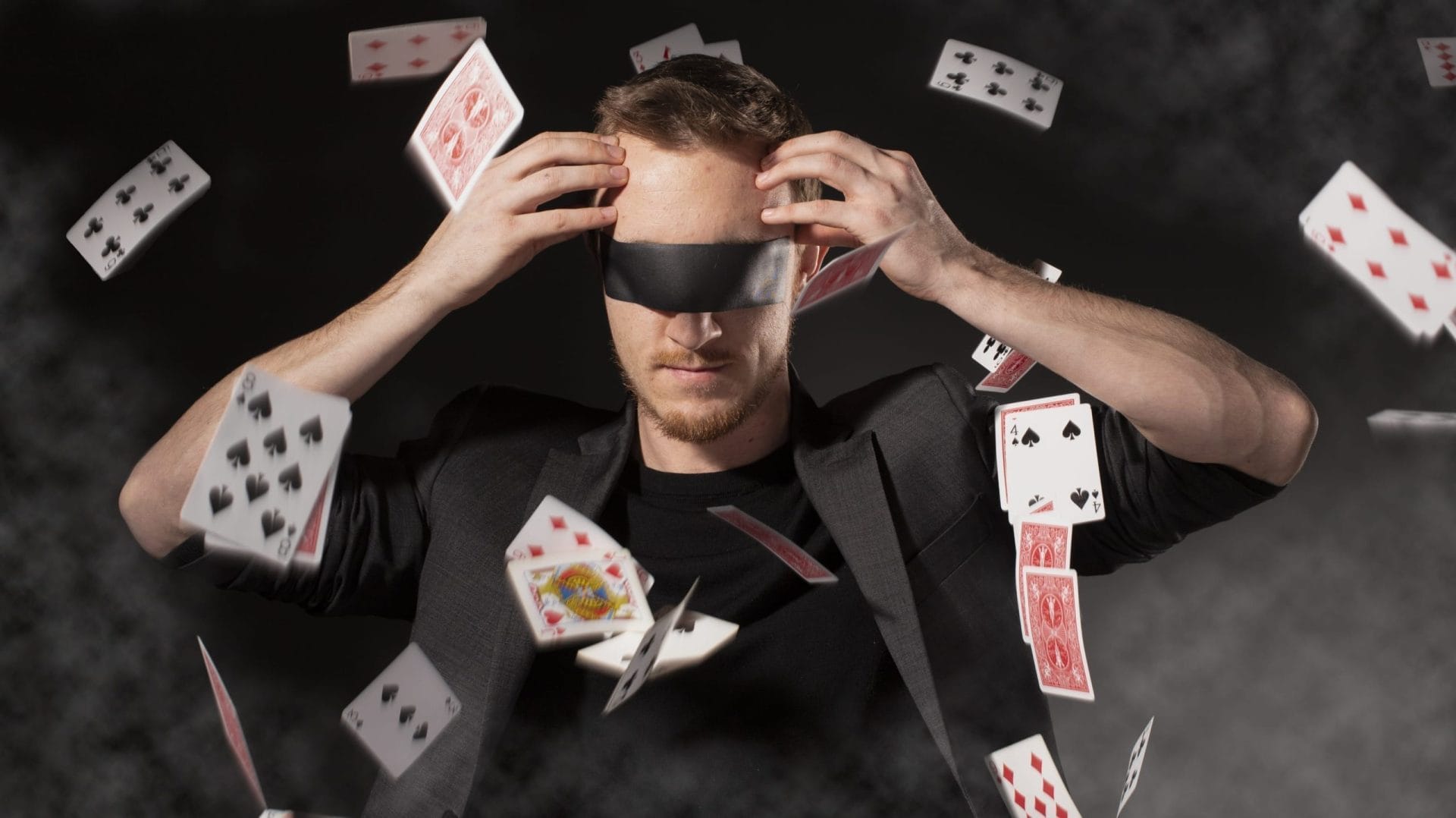 Man blindfolded with playing cards in his hands.