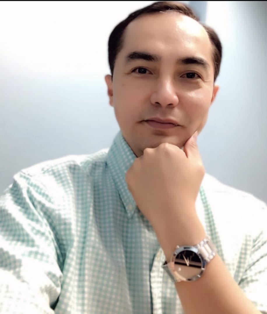 A man in a blue shirt with a watch on his chin.