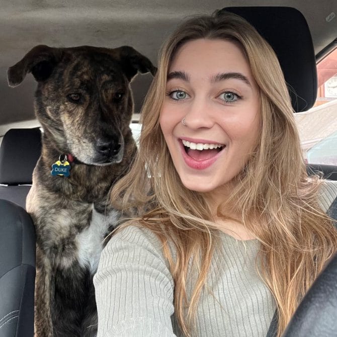 A woman in a car with a dog in the back seat.