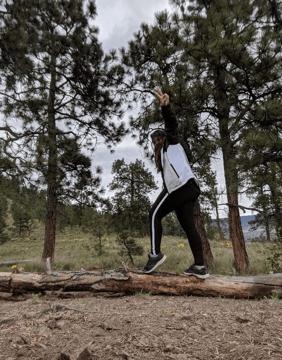 A woman standing on a log in the woods.