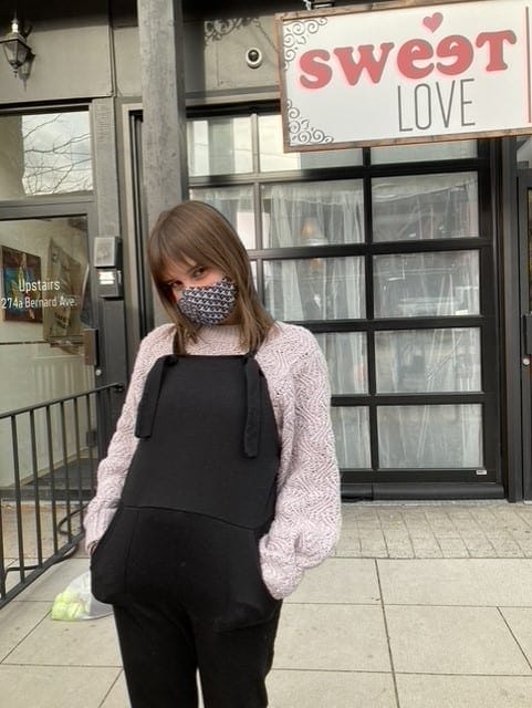 A pregnant woman wearing a mask in front of a sweet love store.