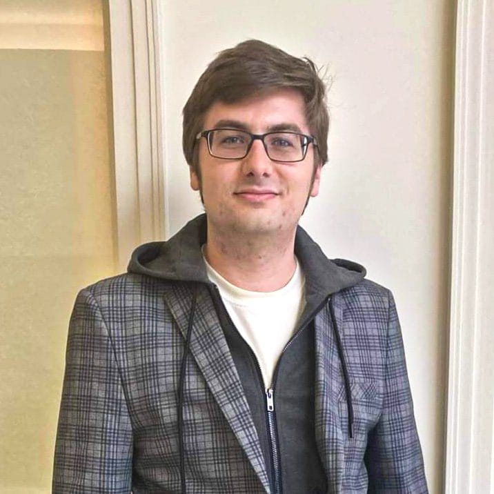 A man in glasses wearing a jacket and a hoodie.