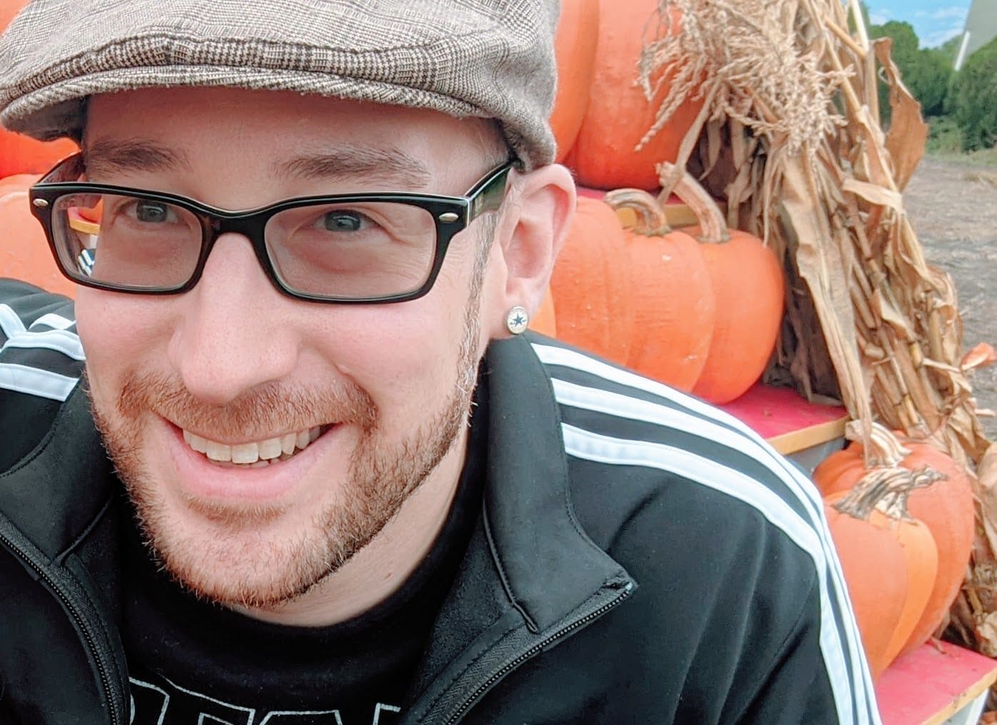 A man wearing glasses and a hat in front of pumpkins.