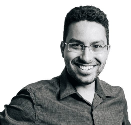 A black and white photo of a smiling man wearing glasses.