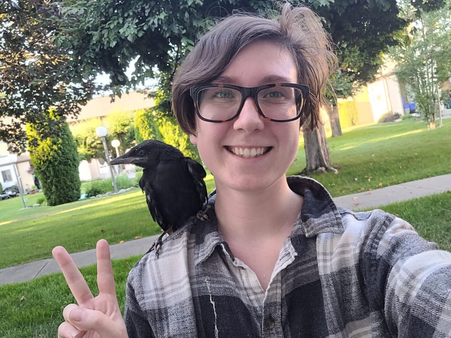 Centre grad Chey Kidd smiles for a selfie with a black bird on their shoulder.  