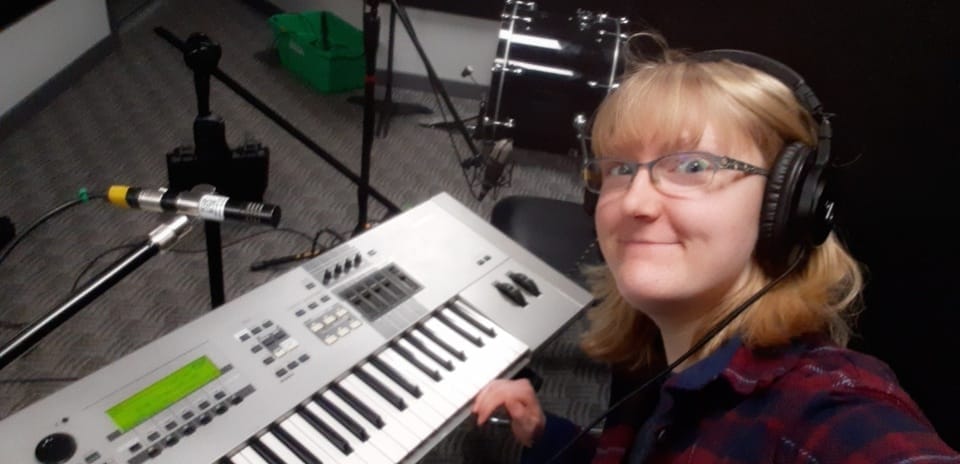 Audio Engineering & Production Grad, Sam McElroy smiles in front of a keyboard.  