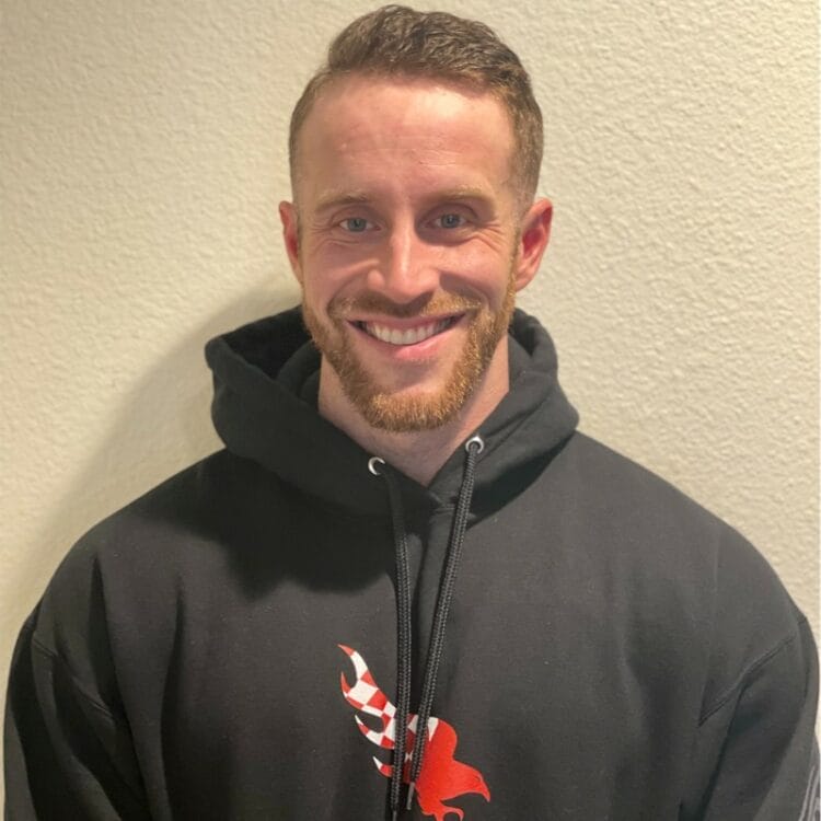 Zach Haight is smiling while wearing a black hoodie with a red logo. They are standing against a plain, light-colored wall, perhaps after a day at the Centre for Arts and Design.